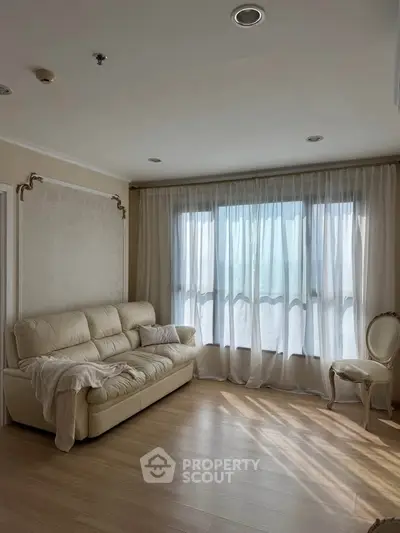 Elegant living room with natural light, featuring a plush sofa and sheer curtains for a cozy ambiance.