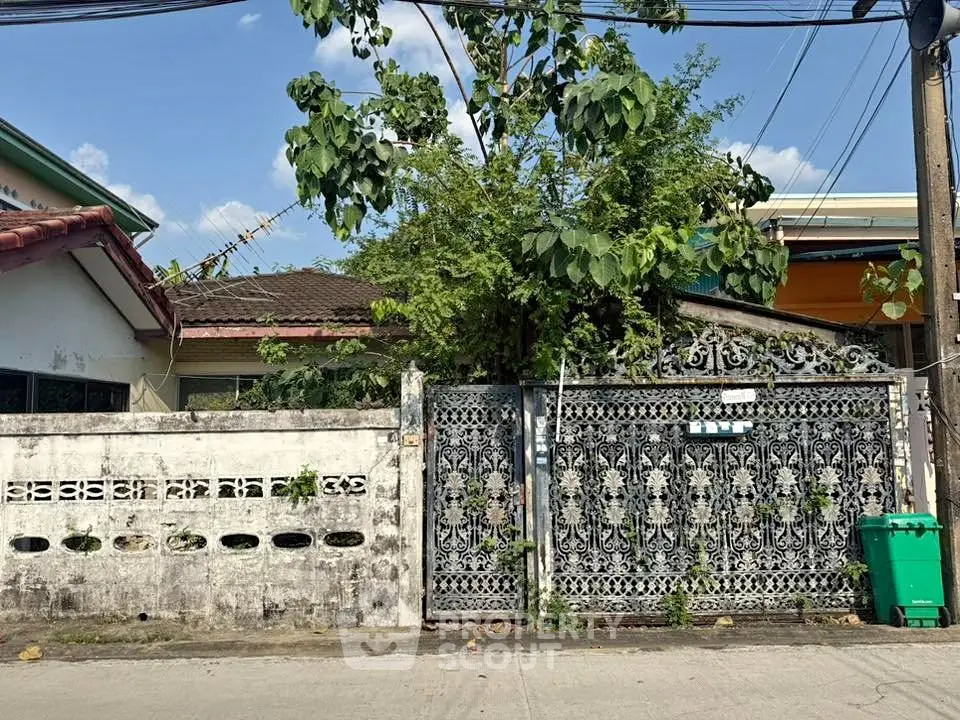 Charming residential property with ornate metal gate and lush greenery, perfect for renovation or investment.