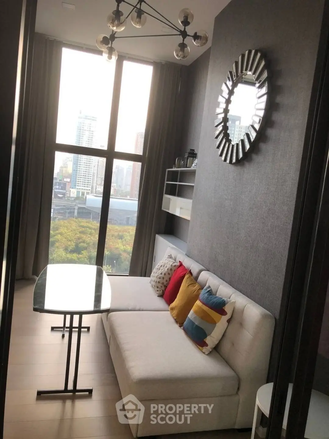 Stylish modern living room with large windows and city view, featuring a cozy sofa and decorative mirror.