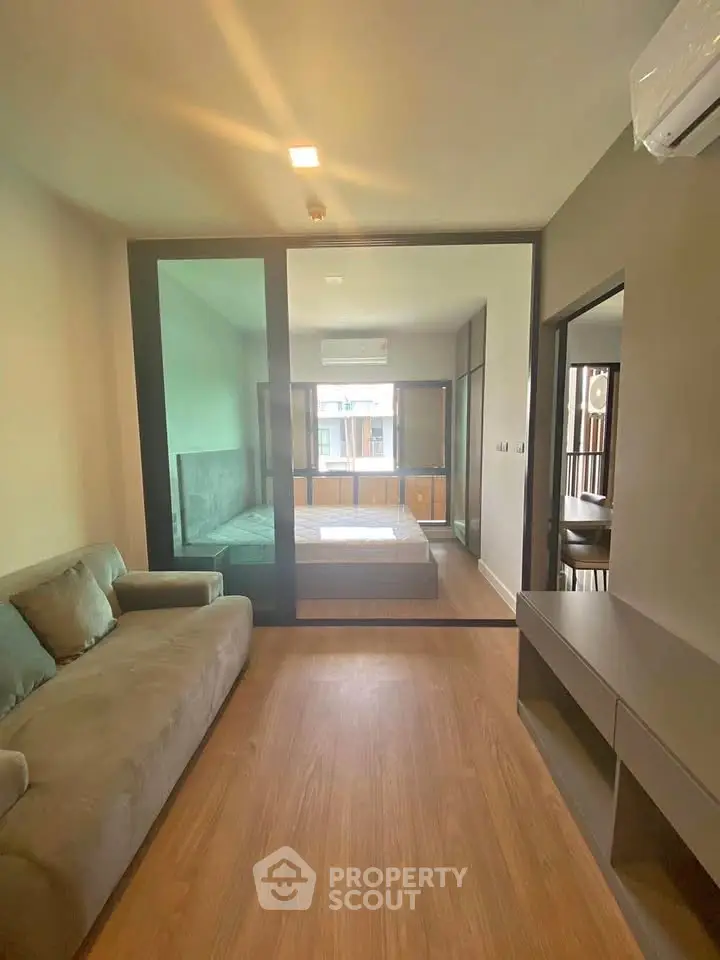 Modern apartment interior with cozy living room and bedroom separated by glass partition.