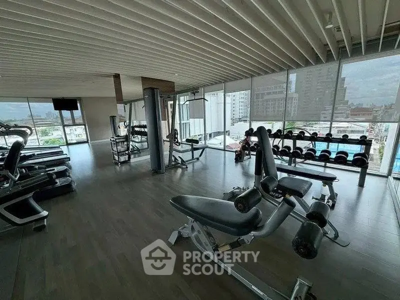 Spacious gym with modern equipment and city view in luxury apartment building.
