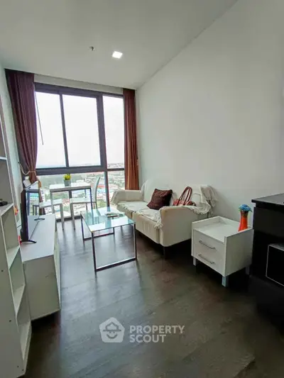 Modern living room with large window and city view, featuring cozy seating and sleek furniture.