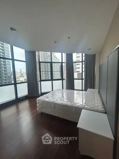 Spacious bedroom with large windows offering stunning city views in a modern high-rise apartment.