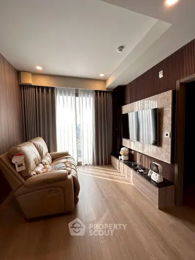Modern living room with cozy sofa and large TV, featuring elegant wooden flooring and natural light.