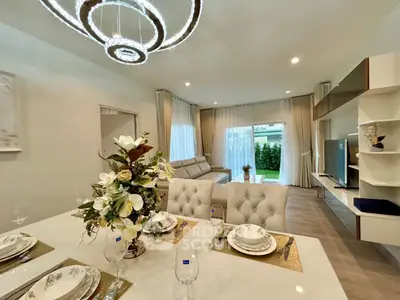 Elegant living room with modern decor and dining area, featuring stylish lighting and garden view.
