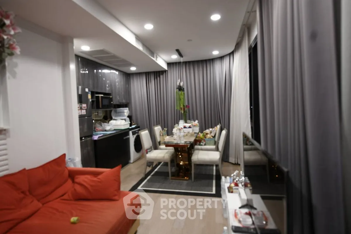 Modern living room with open kitchen, featuring sleek design and cozy seating area.