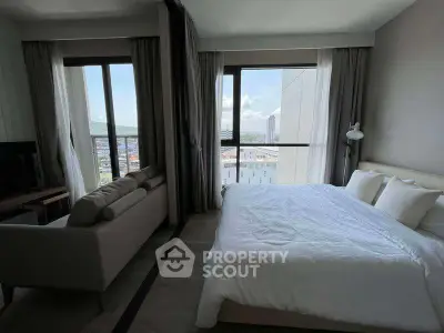 Modern bedroom with large windows offering stunning city views, featuring a cozy bed and stylish sofa.