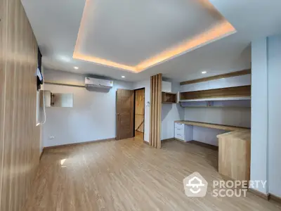 Spacious and modern living room with elegant wooden flooring, ambient cove lighting, and built-in shelving units, perfect for comfortable urban living.