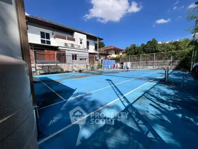 Spacious outdoor tennis court with clear blue sky and residential backdrop