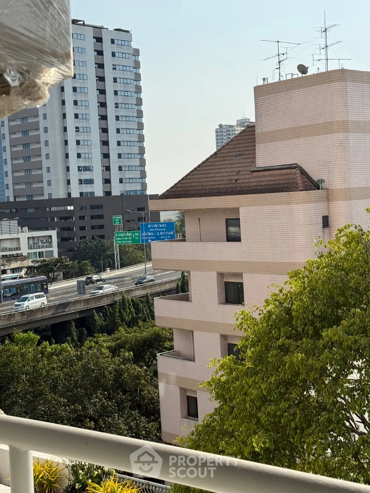 Urban view from balcony overlooking city buildings and highway, showcasing vibrant city life.