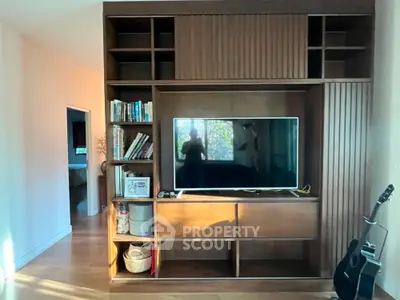 Modern living room with built-in wooden entertainment center and TV, featuring natural light.