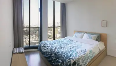 Bright bedroom with large windows and city view, featuring modern decor and cozy bedding.