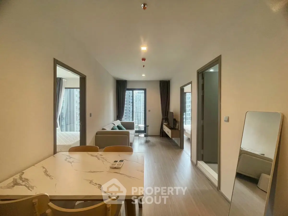 Modern apartment interior with open living and dining area, featuring sleek furniture and large windows.