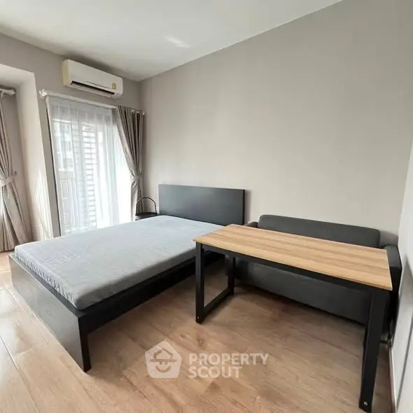 Modern bedroom with minimalist design, featuring a bed, desk, and natural light from large windows.