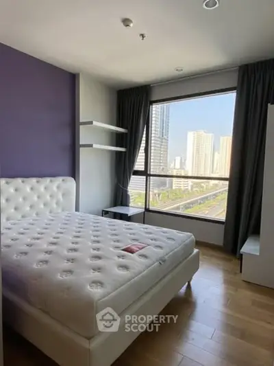 Modern bedroom with large window offering city view, featuring a plush bed and wooden flooring.