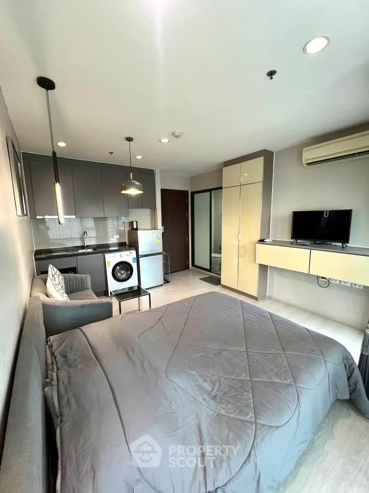 Modern studio apartment with sleek kitchen and cozy living area, featuring a washing machine and stylish decor.