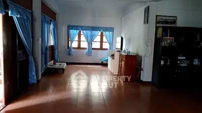 Spacious living room with blue curtains and tiled flooring, featuring a cozy TV corner.