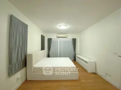 Spacious minimalist bedroom with modern white furniture and wooden flooring.