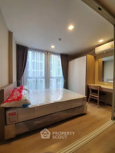 Modern bedroom with large window, wooden flooring, and built-in wardrobe in a stylish apartment.