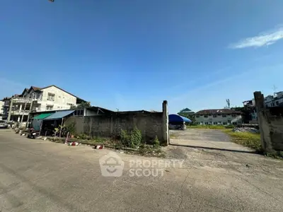 Spacious vacant lot with potential for development, surrounded by residential buildings under clear blue sky.