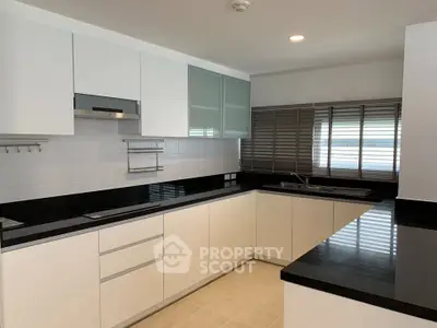Modern kitchen with sleek black countertops and white cabinetry, featuring a closed layout and ample natural light.