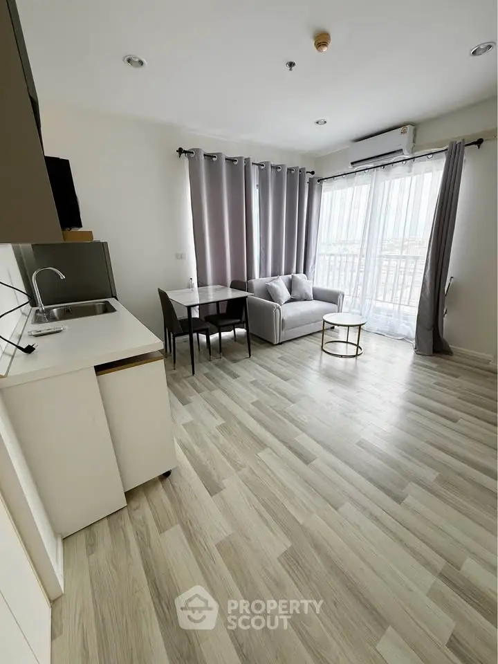 Modern living room with open kitchen and balcony view, featuring sleek design and natural light.