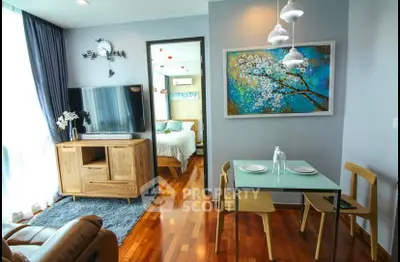 Chic modern living room with wooden floors, stylish furniture, and vibrant artwork, leading to a cozy bedroom.