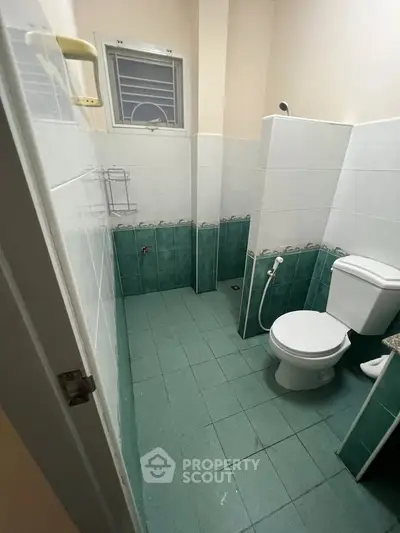 Compact bathroom with green tiles and white fixtures, featuring a toilet and shower area.