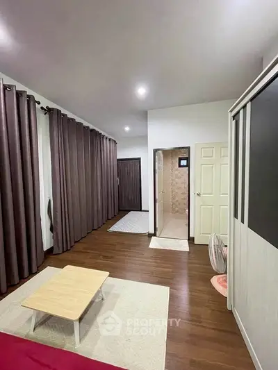 Spacious bedroom with modern decor and ensuite bathroom, featuring elegant curtains and wooden flooring.