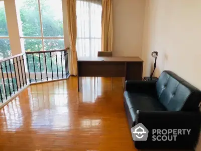 Spacious living room with gleaming hardwood floors, large windows with natural light, and a cozy black leather sofa.