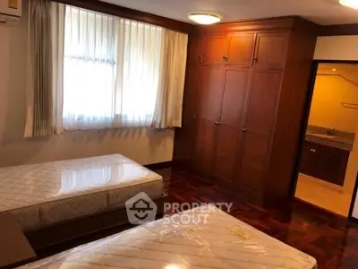 Spacious bedroom with wooden flooring and built-in wardrobe, featuring twin beds and ample natural light.