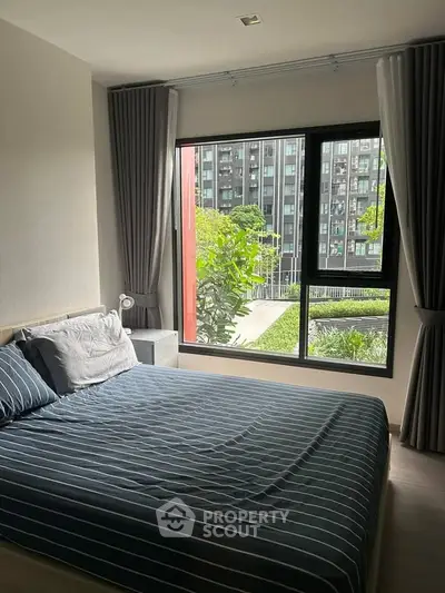 Cozy bedroom with large window offering lush garden view in modern apartment.