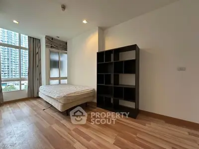 Spacious bedroom with large windows and modern shelving unit in urban apartment.