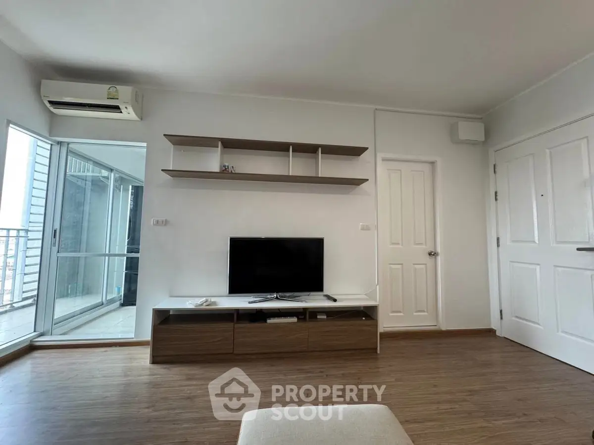 Modern living room with sleek TV unit and balcony access, featuring wooden flooring and minimalist decor.