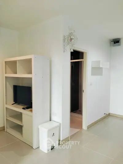 Modern apartment interior with sleek white shelving and wall-mounted TV, leading to a minimalist bathroom.