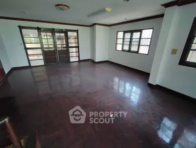 Spacious empty living room with polished wooden floors and large windows.