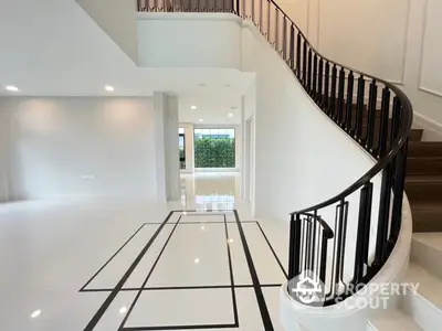 Elegant entryway with a sweeping staircase and high-gloss floors, leading to a bright, spacious living area with modern design.