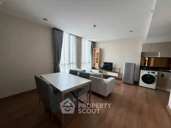 Modern living room with dining area and kitchen featuring washing machine and TV setup.