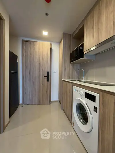 Modern kitchen with wood cabinetry, washing machine, and sleek appliances in a compact layout.