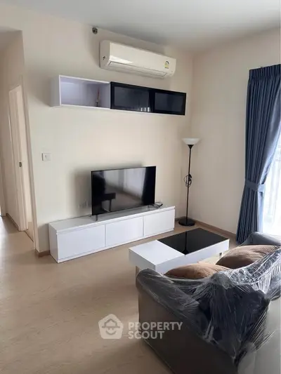 Modern living room with sleek furniture and natural light, featuring a wall-mounted air conditioner and stylish decor.