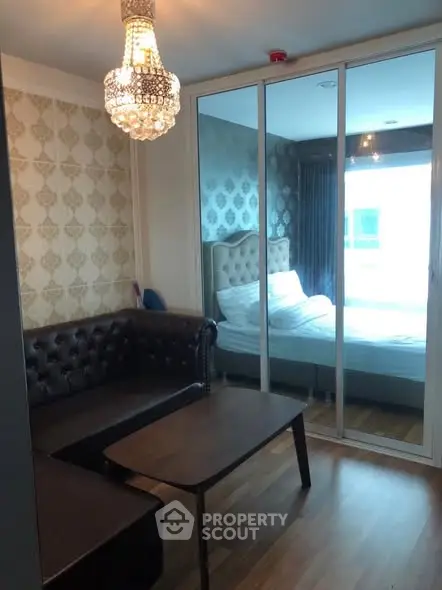 Chic living room with elegant chandelier and mirrored sliding doors leading to cozy bedroom.