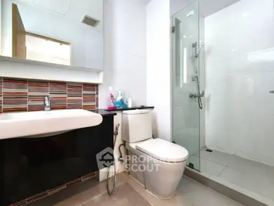 Modern bathroom with sleek fixtures and glass shower enclosure in contemporary apartment.