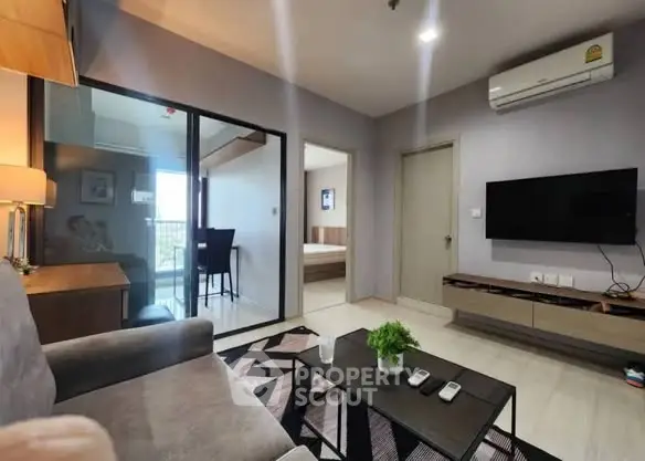 Modern living room with sleek furniture and wall-mounted TV, leading to a balcony with natural light.