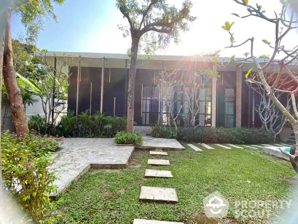 Modern architectural home with lush garden and stone pathway under bright sunlight.