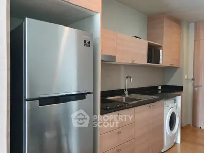Modern kitchen with sleek appliances and wooden cabinetry, featuring a fridge and washing machine.