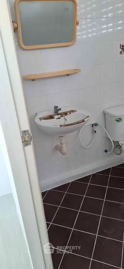 Compact bathroom with wall-mounted sink and tiled floor, ideal for small spaces.