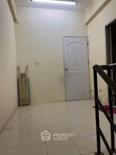 Spacious interior hallway with tiled flooring and a closed door, ideal for storage or utility use.