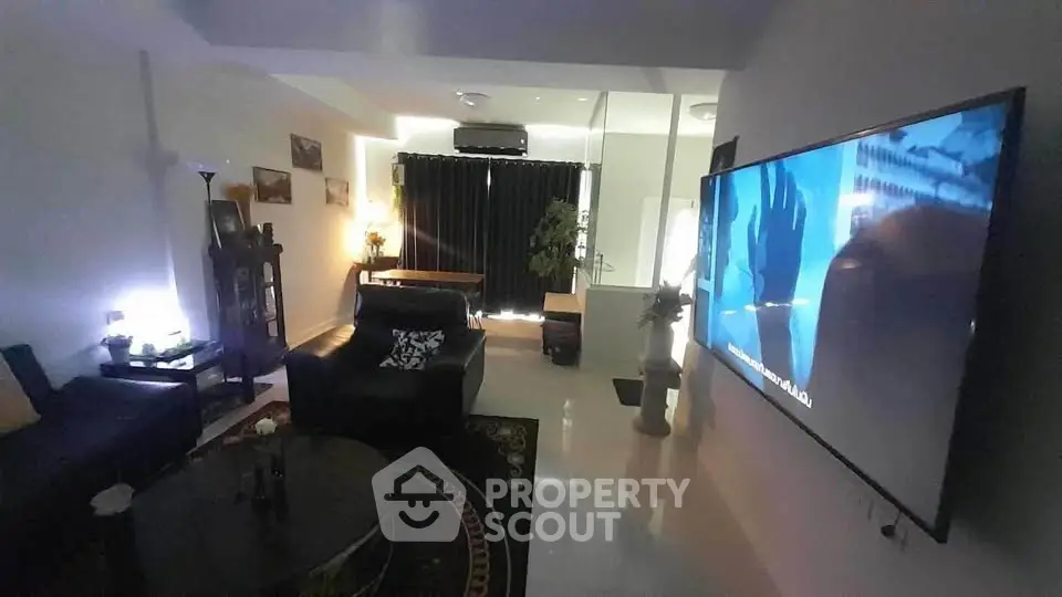 Modern living room with large TV and stylish decor, featuring cozy seating and ambient lighting.
