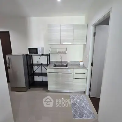 Modern kitchen with sleek cabinetry, stainless steel fridge, and microwave in a compact layout.