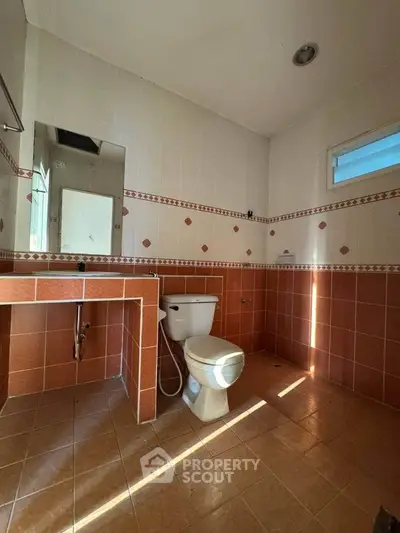 Spacious bathroom with tiled walls and floor, featuring a toilet and mirror, ideal for modern living.